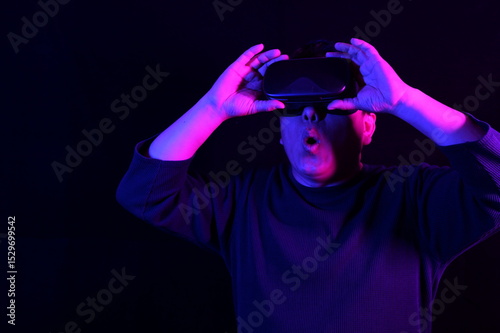 A person wearing a VR headset, with hands raised as if interacting with a virtual environment, illuminated by blue and pink neon lights against a dark background