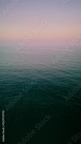 A peaceful drone flight over the Mediterranean Sea near Alicante, Spain, transitioning slowly to reveal the shoreline, sandy beach, and city skyline under soft sunset light. 