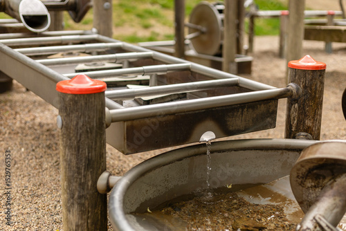 Fototapeta Naklejka Na Ścianę i Meble -  A water play station at a playground invites children to explore and engage with flowing water. Kids can observe the movement of water while playing with the interactive features and elements