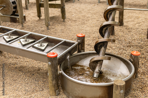Children engage with interactive water play equipment featuring a spiral water screw and a water basin, encouraging hands-on learning and exploration in a bright playground
