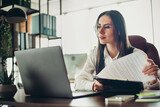 Professional businesswoman in formal attire working diligently at her office desk, reviewing documents and focusing on tasks.
