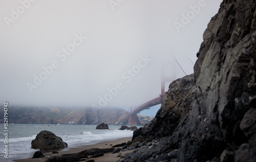 The Golden Gate Bridge in San Francisco, California disappears into the fog, as seen from the beach.