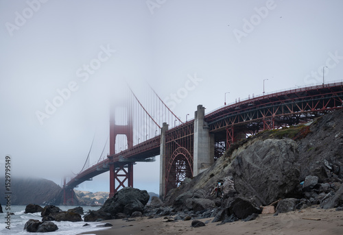 The Golden Gate Bridge in San Francisco, California disappears into the fog, as seen from the beach.
