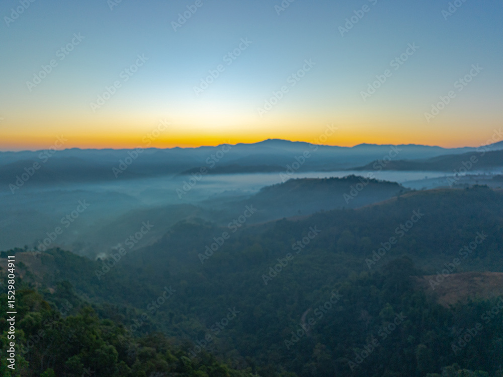 Obraz premium Aerial view of A breathtaking aerial view of a lush, green mountain range under a bright, clear blue sky, with sunlight illuminating the vast, rolling terrain and valleys below.