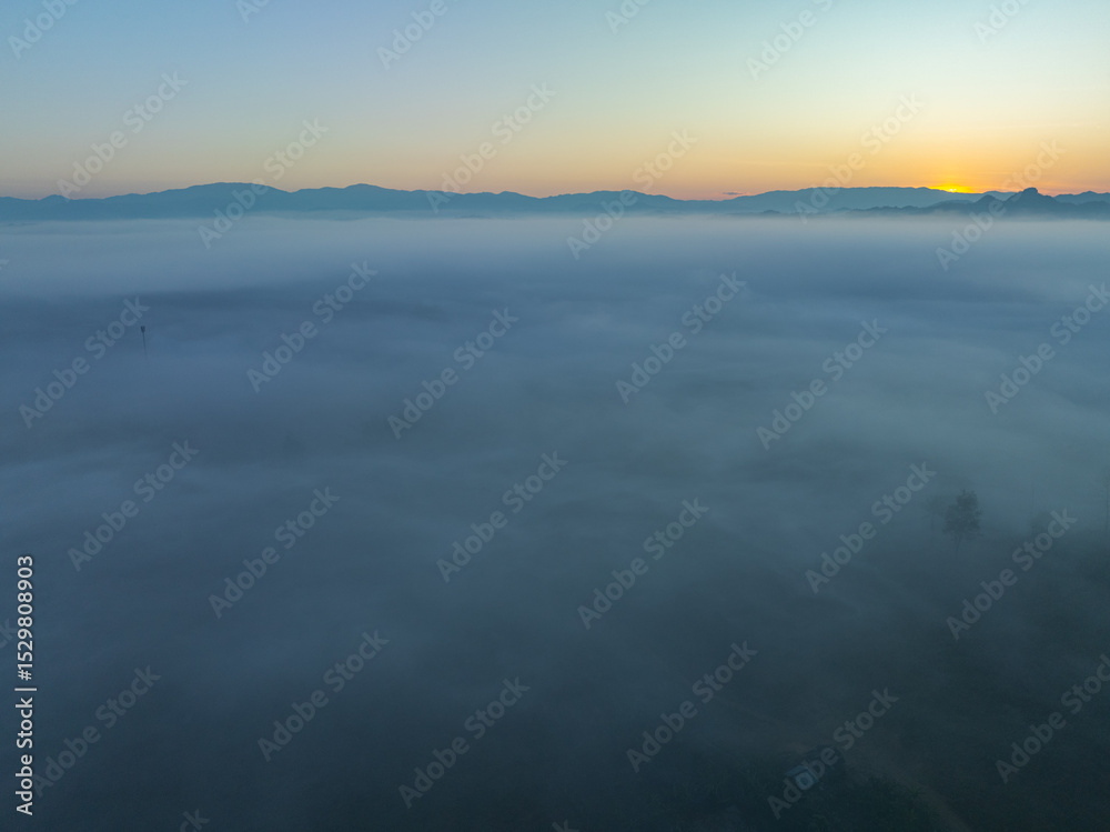 Fototapeta premium aerial view a sea of white mist envelops the mountain peak, slowly flowing down from the mountain peak. The mist poured down from the mountains in the morning. the sea of mist background.