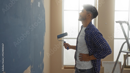 Quadro su tela Young hispanic man painting wall in modern home interior, holding roller brush w