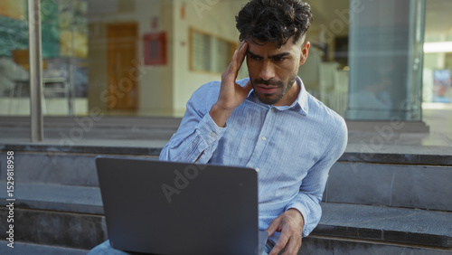 Man outdoors looking concerned while sitting on city steps with open laptop showcasing urban lifestyle and technology challenges in a public space during daytime.