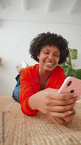 Joyful female enjoying her time while lying on the floor and using her smartphone to communicate with friends through various applications or social media platforms, feeling relaxed and connected