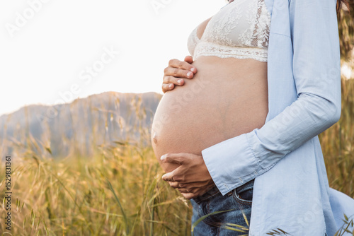 Close-up of pregnant belly in soft natural light with hands embracing. Lifestyle. photo