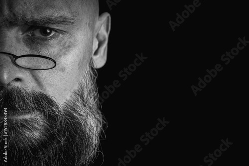 Funny close-up of a weird bald man with a long gray beard and glasses making a funny face, half face. Concept of eccentricity, humor and expressive personality.