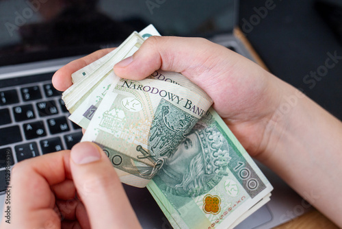 Holding Polish Zloty Bills Near Laptop