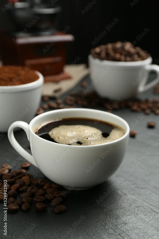 Fototapeta premium Cup of drink, ground coffee and beans on black table, closeup