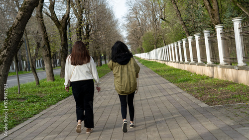 Two women walking on a tree-lined sidewalk during daytime in a peaceful urban area