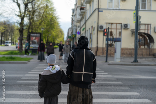 Mother and child crossing the street on a sunny day in a busy urban area
