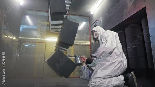 Painter in protective suit spraying metal parts in booth, industrial coating process, Powder coat application for corrosion resistance and surface durability