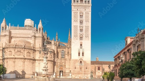 Panorama showing the Seville Cathedral and Giralda Tower timelapse hyperlapse in Seville, Spain. The largest gothic cathedral in the world, located on Virgen de los Reyes square under a blue sky