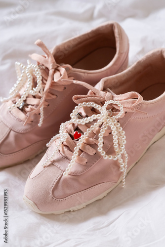Pink sneakers with pearl bead bow on white sheet, trendy footwear