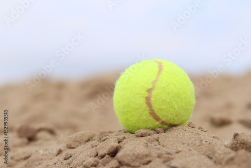Yellow tennis ball lies on the sand. Sports and recreation concept, summer games. Tennis or paddleball ball. Tennis court near the beach. Paddleball ball on the sand near the water. Outdoor games