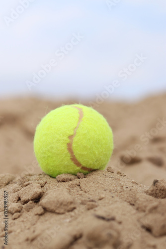Yellow tennis ball lies on the sand. Sports and recreation concept, summer games. Tennis or paddleball ball. Tennis court near the beach. Paddleball ball on the sand near the water. Outdoor games