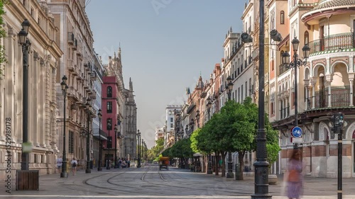 Pedestrians walking along Avda. de la Constitucion, major avenue in Casco Antiguo district of Seville, Spain. Timelapse near Edificio de la Adriatica, historical buildings and passing trams