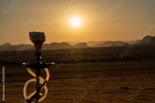 Hookah in the Desert Sunset: A solitary hookah stands silhouetted against a majestic desert sunset, capturing the tranquility and mystique of the vast, open landscape.