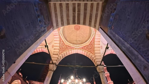 A detailed view of an illuminated architectural archway with carvings, showcasing the dome and minaret in the background at night in Sultanahmet Blue Mosque