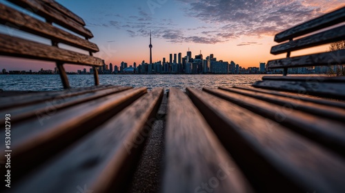 View of a vibrant city skyline captured through wooden slats, showcasing the towers and buildings as the sun sets over the water, creating a picturesque moment