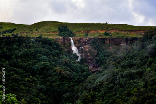 Dramatic Dainthlen waterfall cascades down a rocky cliff amidst lush green foliage.