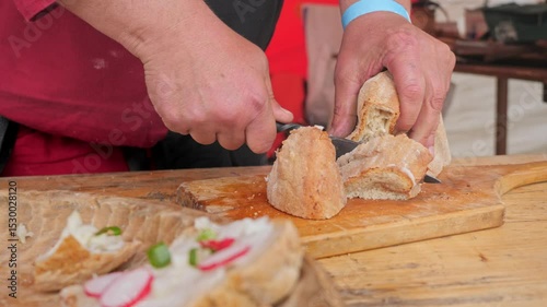 cutting bread with a historical decorated metal knife on a wooden board with garnished bread in te foreground