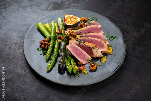 Tuna tataki steak with caramelized green asparagus, roasted cashew and  maracuja passion fruit relish dip sauce served as close-up on a design plate