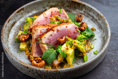 Tuna tataki steak with avacado, roasted cashew, chuka wakame and maracuja passion fruit relish dip sauce served as close-up on a design plate