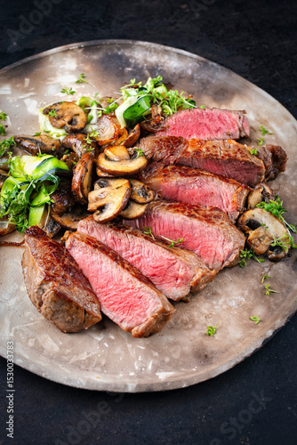 Traditional barbecue grass-fed dry aged roast beef steak  with mushrooms and greens served as close-up on a rustic design plate