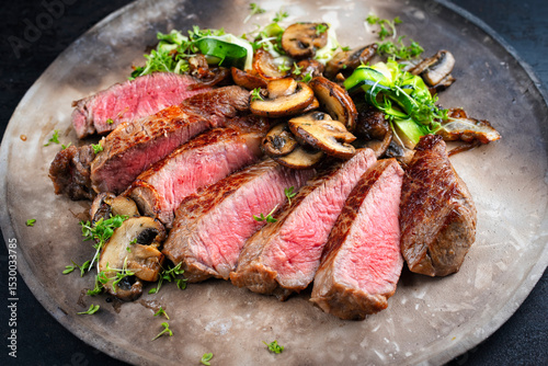 Traditional barbecue grass-fed dry aged roast beef steak  with mushrooms and greens served as close-up on a rustic design plate