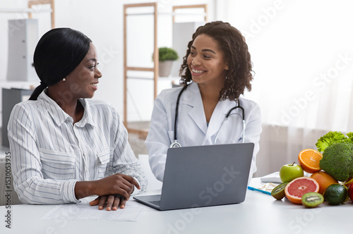 Smiling black lady doctor chatting with female patient at clinic, dietology and nutririon concept photo