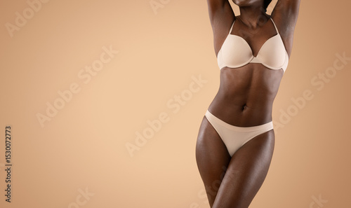 Attractive slender black lady with hands up posing in underwear over beige studio background, showing her beautiful curves, cropped, panorama with copy space. Diet, athletic body concept