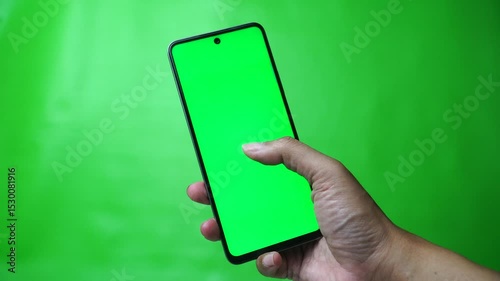 Hand holding smartphone with chroma green screen, finger swiping screen. Green background
