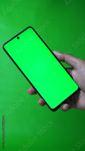 Hand holding smartphone with chroma green screen, finger swiping screen. Green background