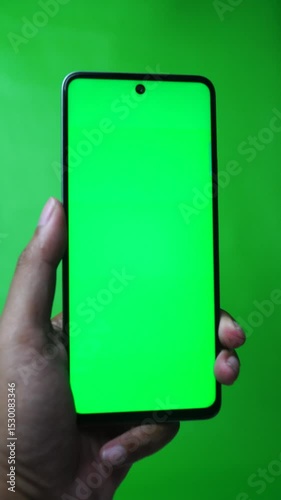 Hand holding smartphone with chroma green screen, finger swiping screen. Green background