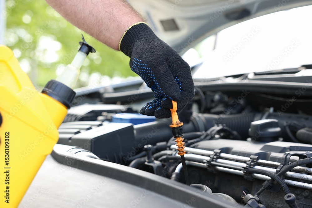 Fototapeta premium Worker checking motor oil level in car with dipstick, closeup