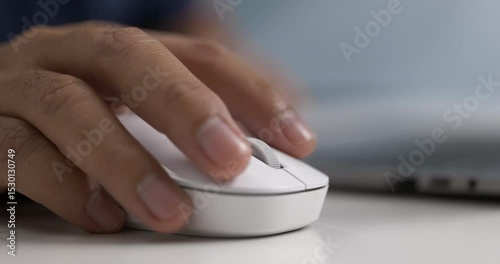 Close-up of hand using white wireless mouse near laptop on modern white desk.
