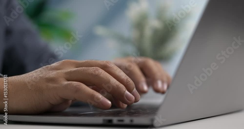 Fingers typing on sleek laptop keyboard with soft daylight in modern workspace.