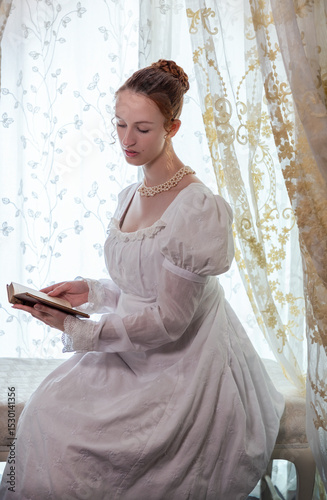 A Regency period woman wearing a white embroidered cotton dress and surrounded by backlit lace curtains