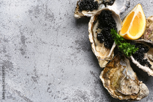Tasty oysters with lemon and black caviar on grey background