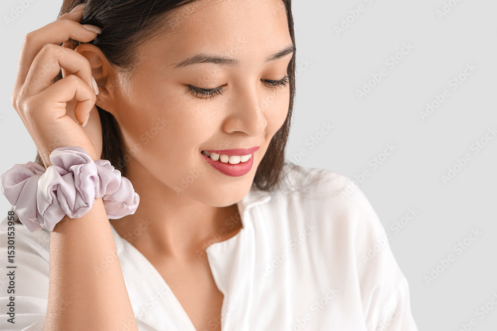 Young Asian woman with scrunchy on light grey background, closeup Young Asian woman with scrunchy on light grey background, closeup