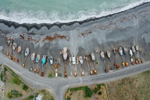 Aerial view of boats and tractors parked on a black sand beach in Ngawi, Cape Palliser, Wellington, New Zealand. The boats are being stored for the off-season, protected from the ocean waves. photo