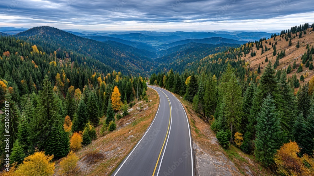 Fototapeta premium Scenic mountain road winding through colorful forested hills under a cloudy sky