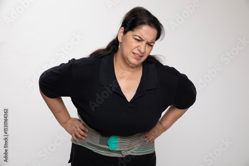 Indian matured senior woman wearing back support belt on white background. Concept of back pain