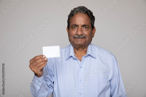 Portrait of an indian senior man holding Aadhar card on grey studio background