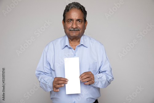Portrait of an indian senior man holding Aadhar card on grey studio background