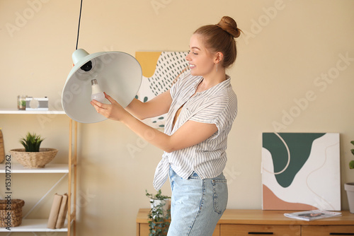 Young woman screwing light bulb into ceiling lamp at home